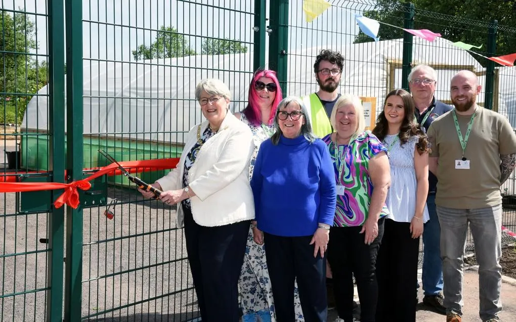 Group of staff beside entrance as one person cuts a red ribbon to officially open a community garden space.