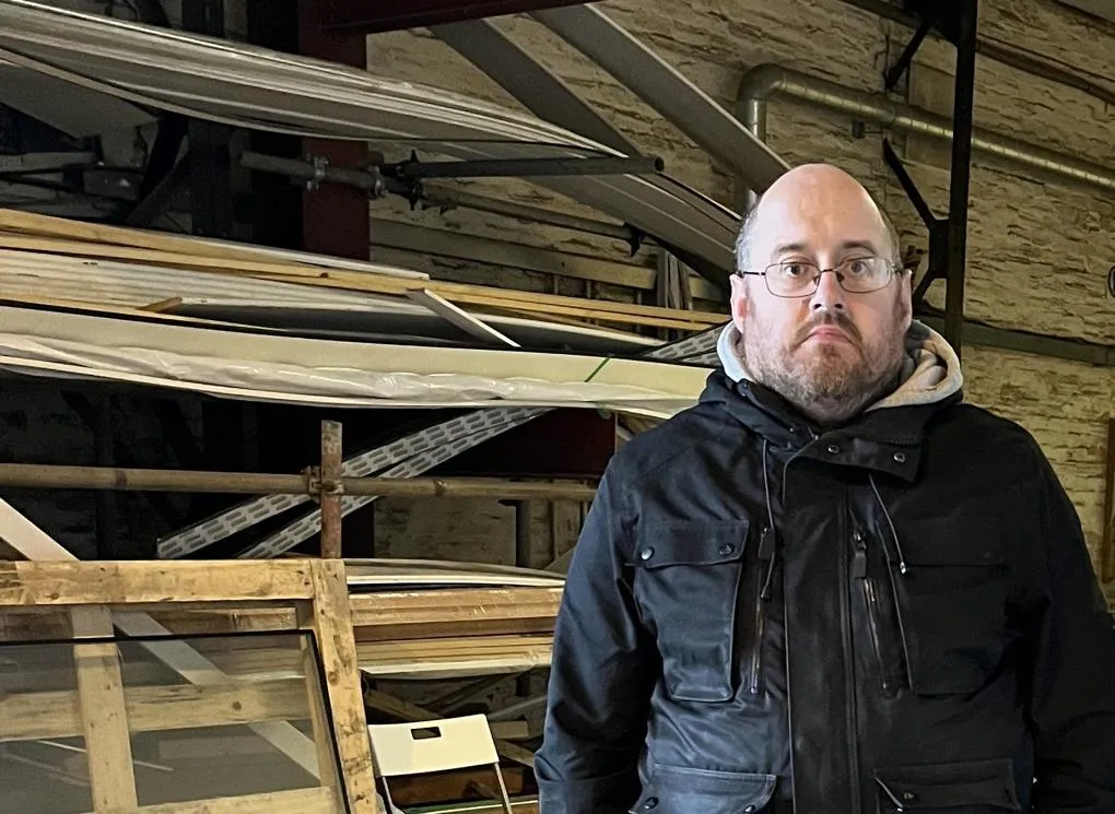 A man standing in front of some shelves of assorted wood