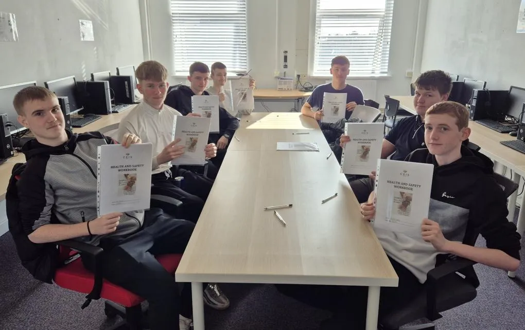 Young people sitting around a table, each holding a health and safety workbook